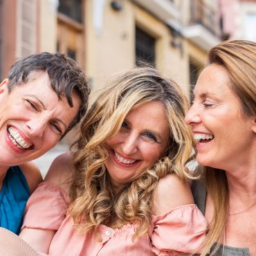 Three laughing mature friends together looking at the camera. Middle aged friends sharing time together and having fun.