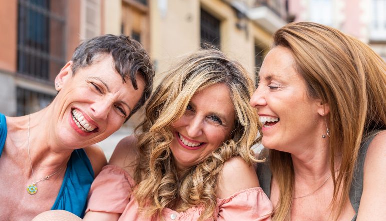 Three laughing mature friends together looking at the camera Three laughing mature friends together looking at the camera. Middle aged friends sharing time together and having fun.